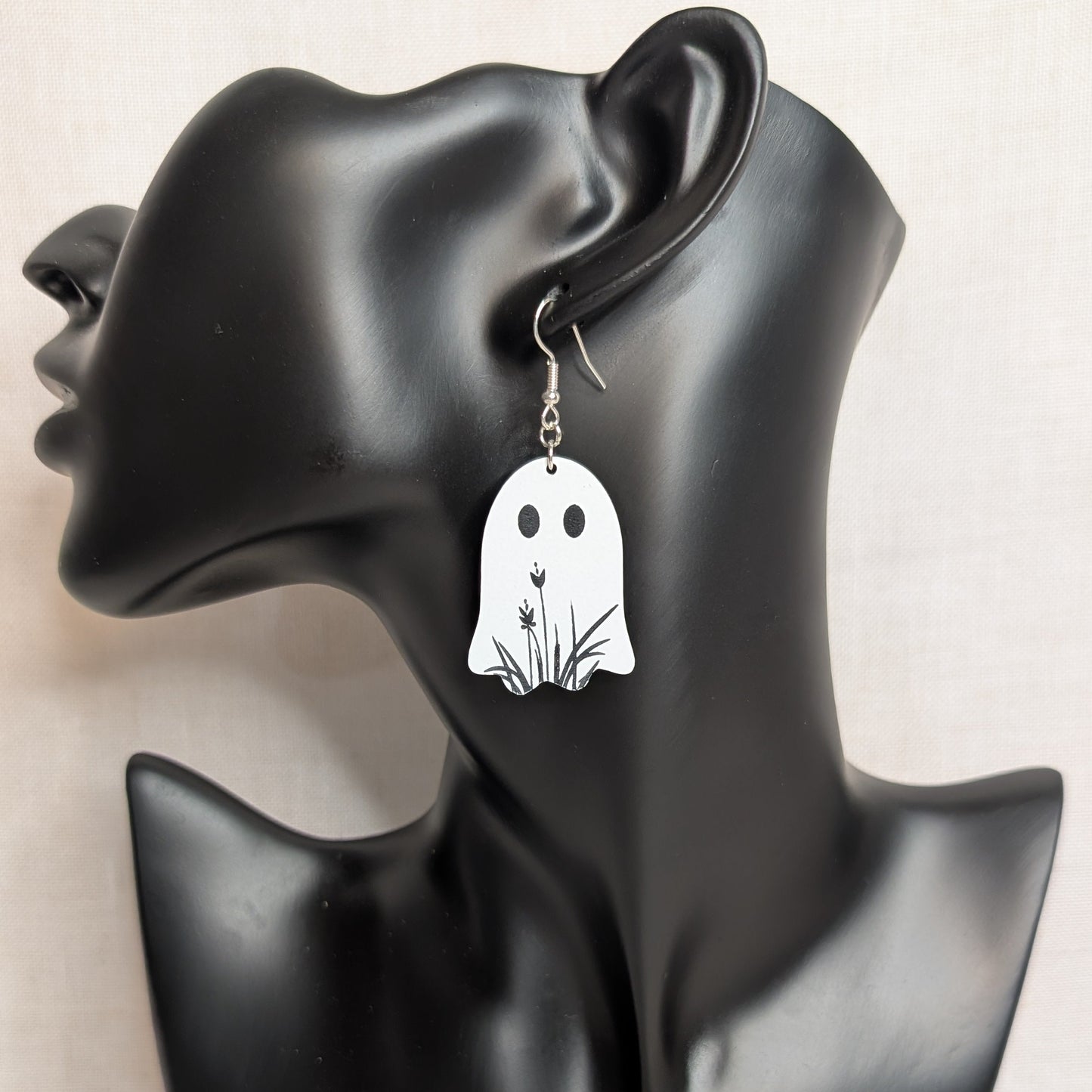 White floral ghost dangle earring displayed on a black jewelry stand, handmade Halloween accessory.