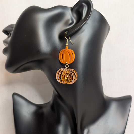 Orange double pumpkin dangle earring with glitter detail displayed on a black jewelry stand for fall and Halloween.