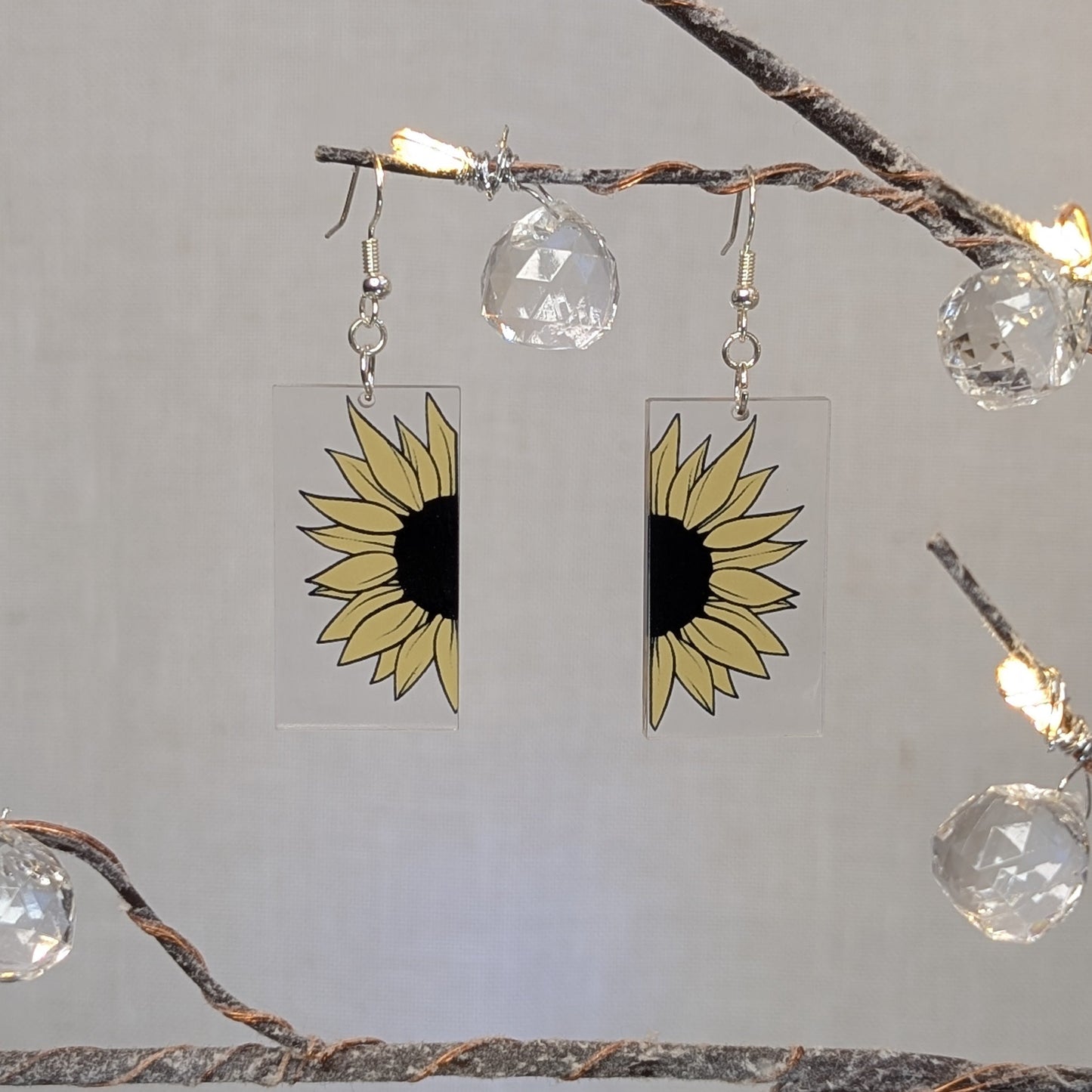 Pair of bright cheerful sunflower earrings printed on clear rectangular acrylic with yellow petals and black centers.