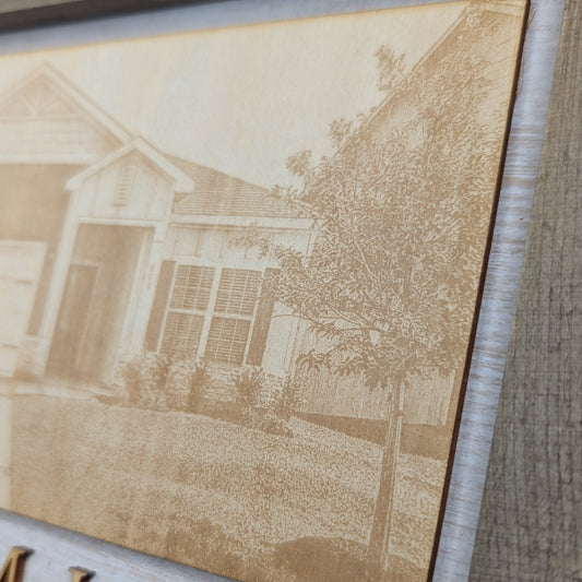 Close-up detail of a custom engraved home portrait in a rustic wood frame, featuring a personalized house illustration and address with precision laser engraving.