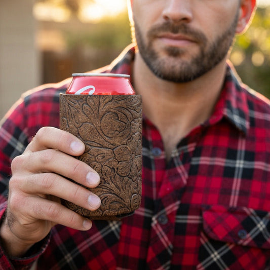 Man holding a red beverage can in a brown embossed floral leather koozie outdoors.