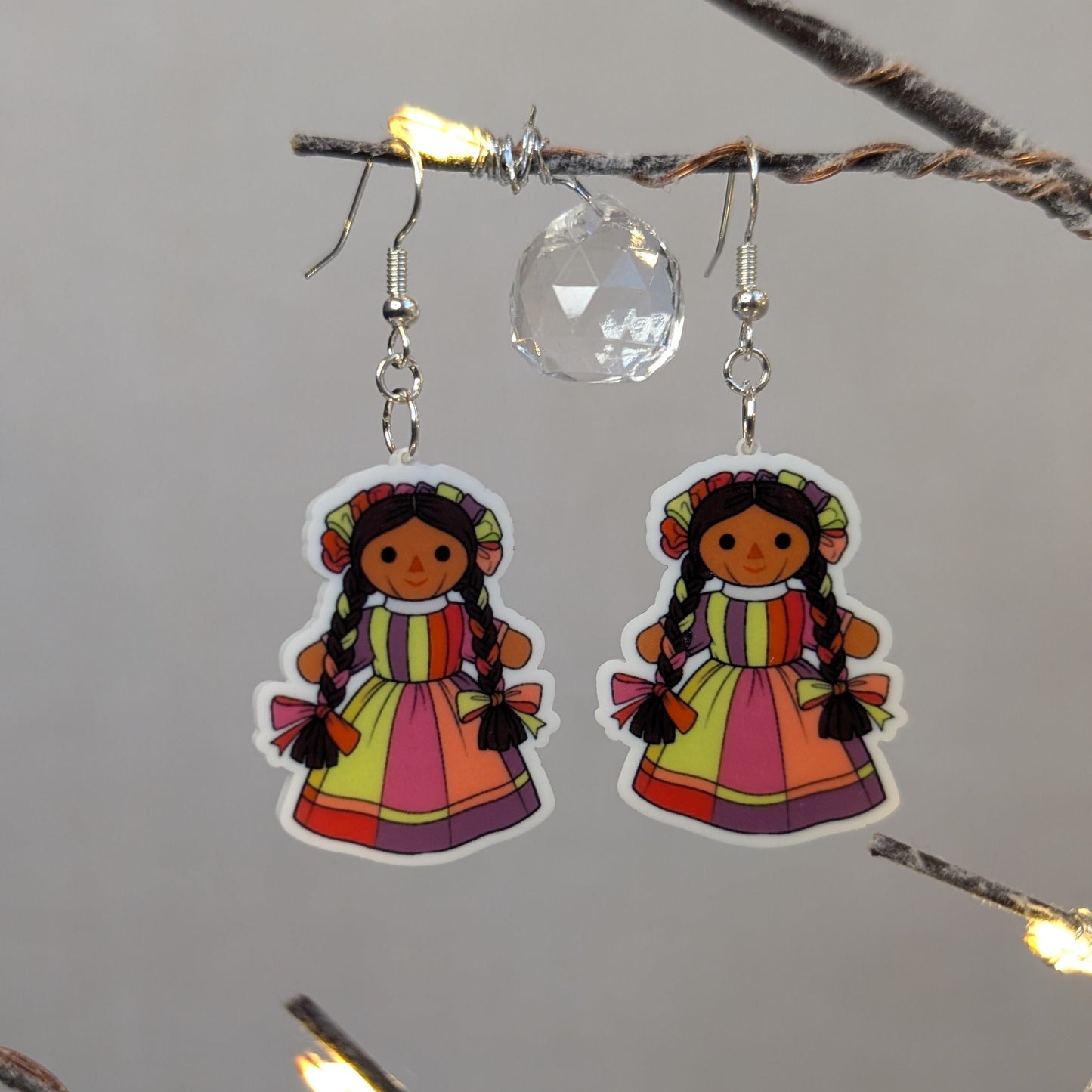 Pair of colorful Muñeca Mexican doll acrylic dangle earrings with braided hair and bright traditional dresses.