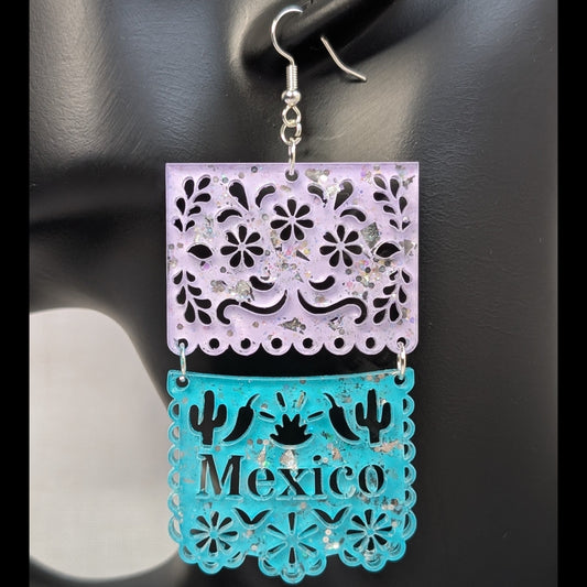 Close-up of turquoise and pink Papel Picado Mexico dangle earring with floral cutouts and cactus details.