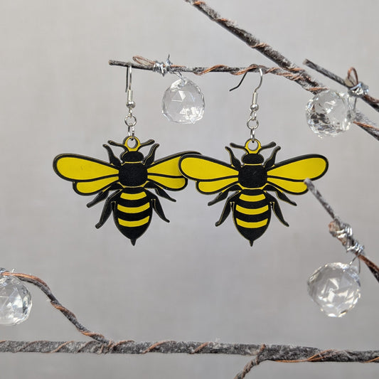 Yellow and black Sweet Buzz-Worthy Bee dangle earrings with detailed wings and striped bodies displayed on a decorative branch.