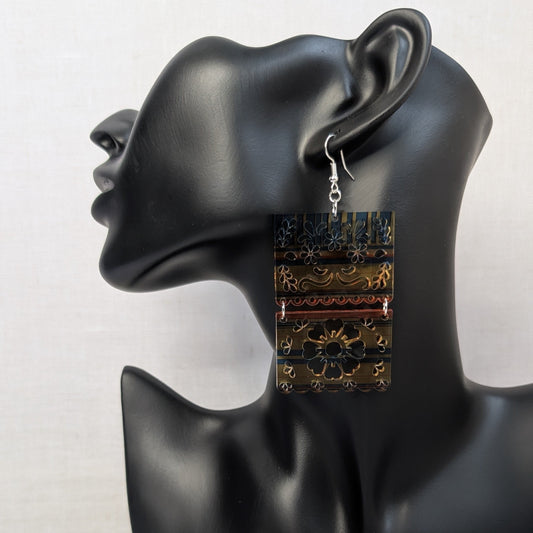 Sarape Earrings Flower. Colorful rectangular floral dangle earring with blue, yellow, orange, and white patterns displayed on a black jewelry mannequin.