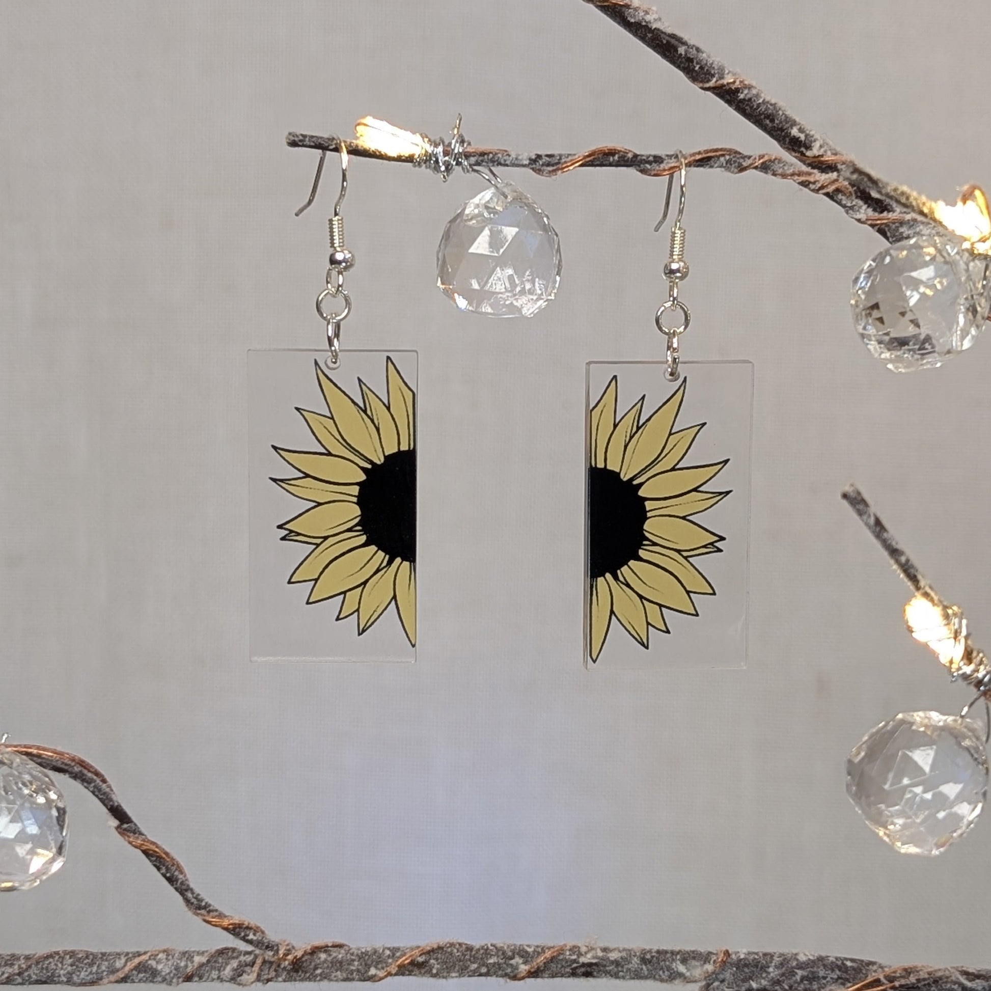 Pair of bright cheerful sunflower earrings printed on clear rectangular acrylic with yellow petals and black centers.