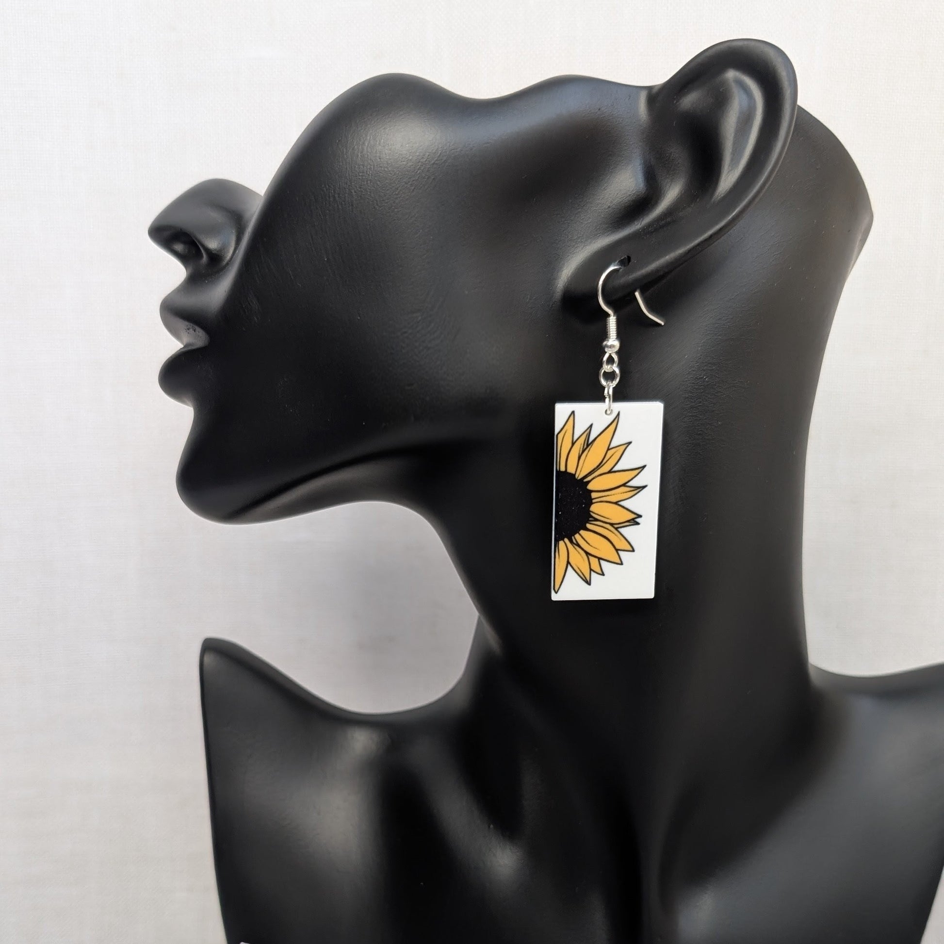Bright and cheerful sunflower dangle earring with yellow petals and a black center displayed on a black jewelry stand.