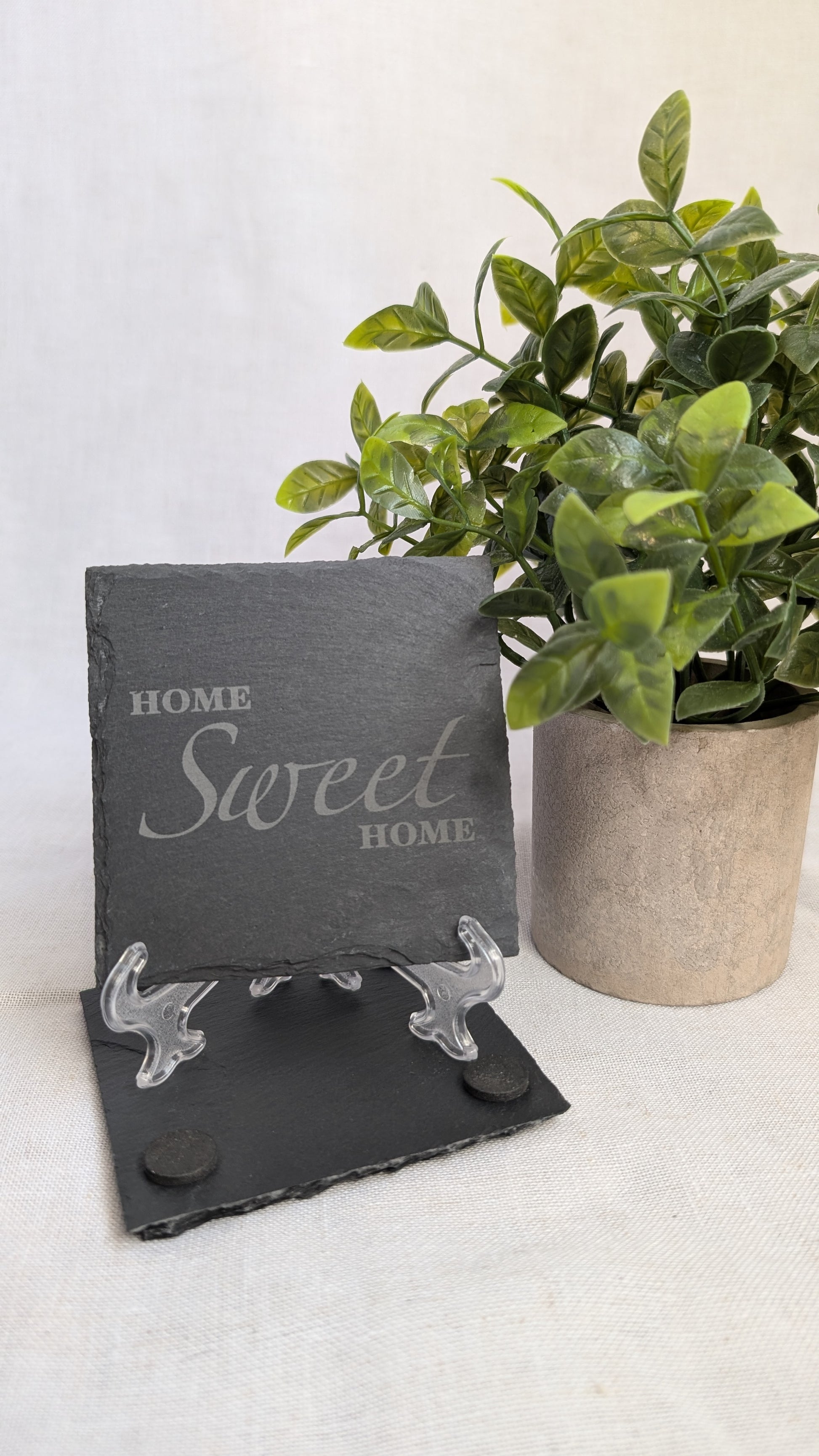 Engraved slate coaster featuring a "Home Sweet Home" design displayed on a stand beside a decorative plant, perfect for housewarming gifts and personalized home décor.