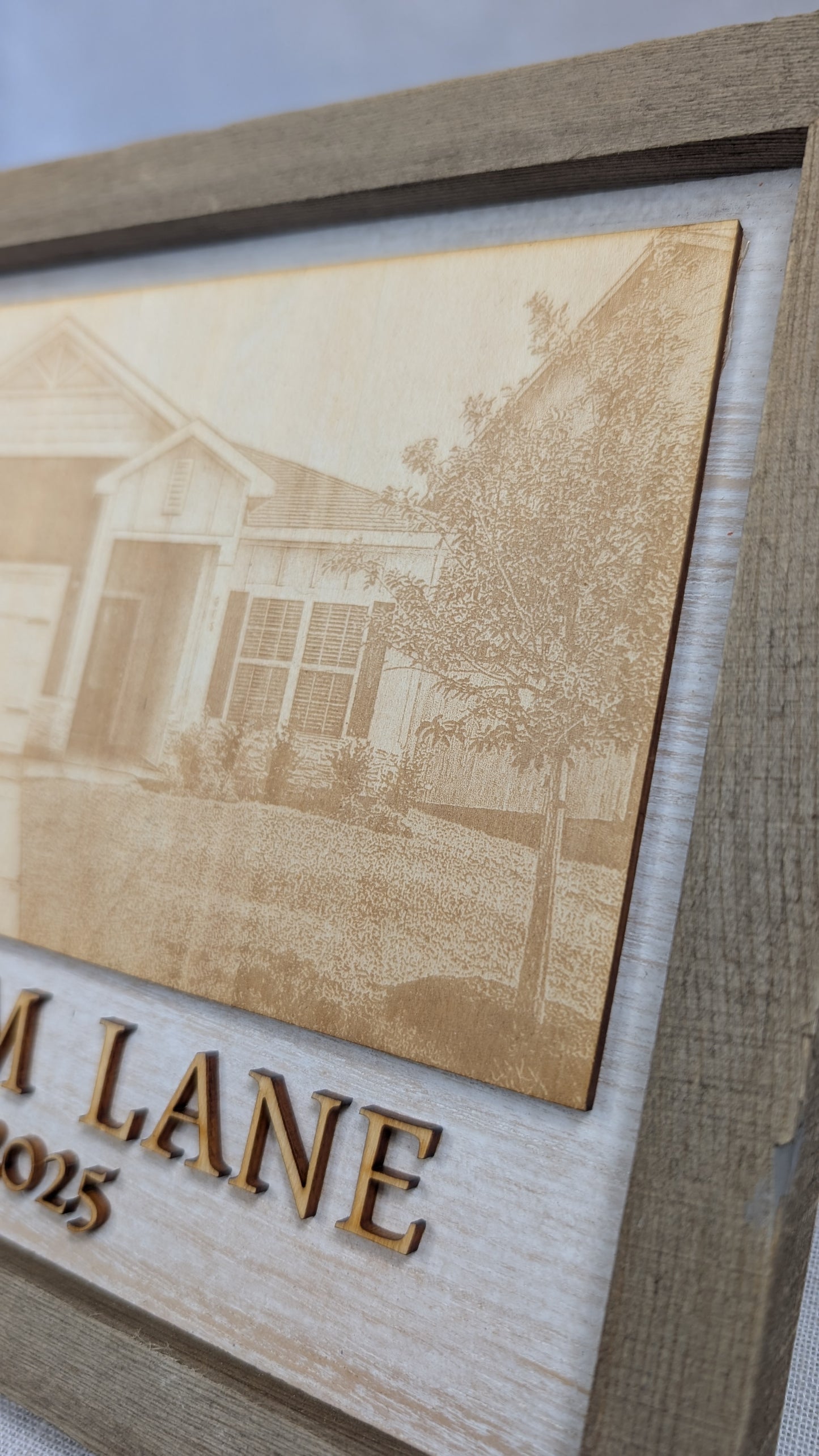 Close-up detail of a custom engraved home portrait in a rustic wood frame, featuring a personalized house illustration and address with precision laser engraving.