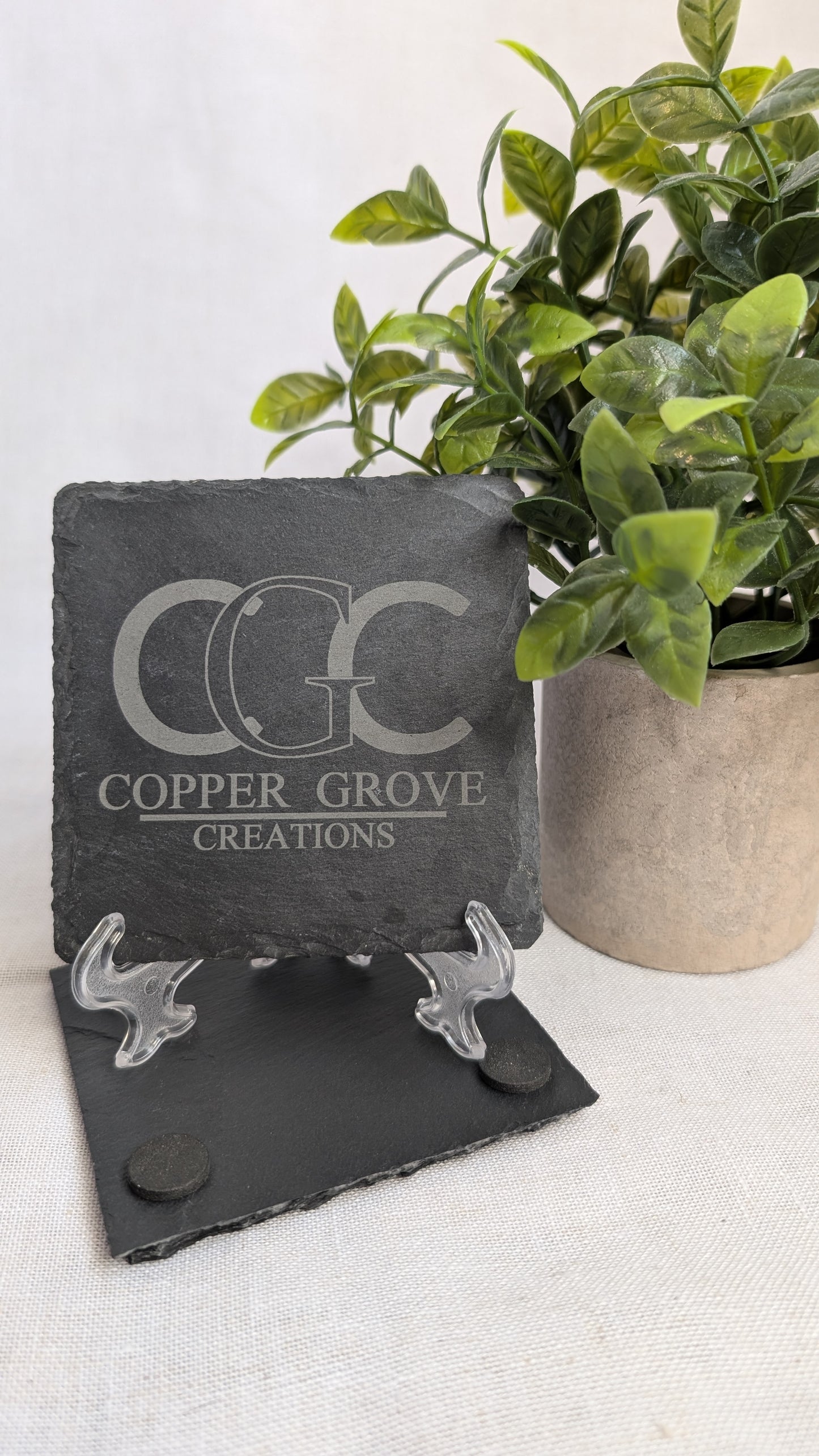 Custom engraved slate coaster featuring the Copper Grove Creations logo, displayed on a stand to showcase detailed laser engraving and natural stone texture.