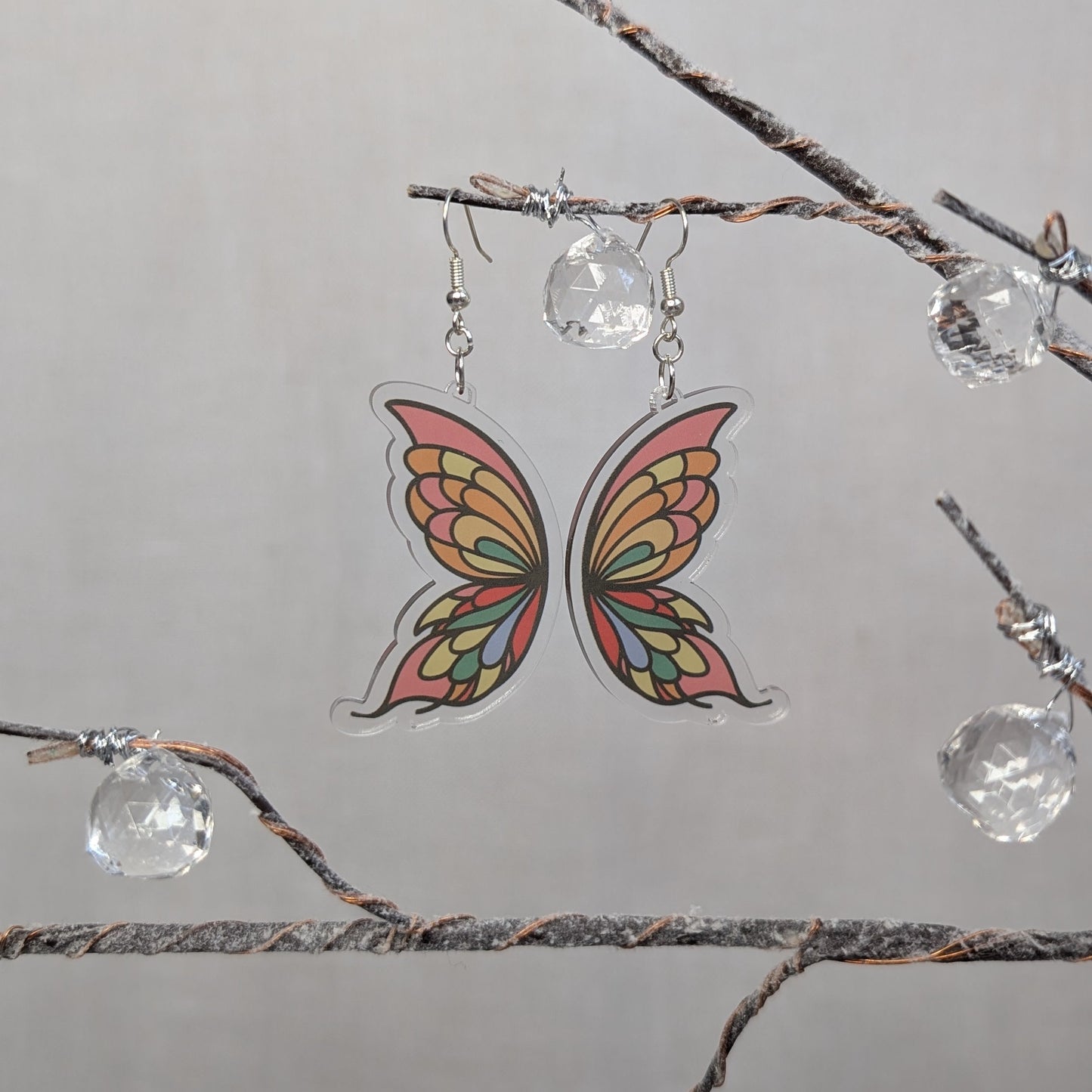 Delicate butterfly wing earrings with colorful orange, yellow, green, and pink details on clear acrylic.