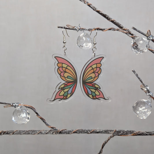 Delicate butterfly wing earrings with colorful orange, yellow, green, and pink details on clear acrylic.