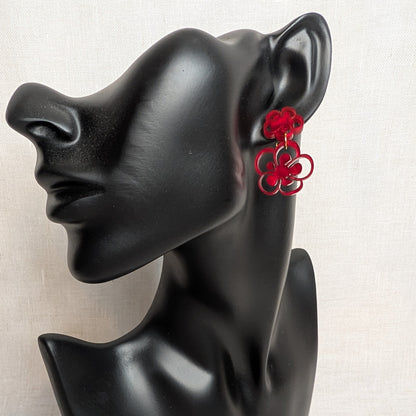 Red marbled flower bloom acrylic dangle earring with layered floral shapes displayed on a black jewelry stand.