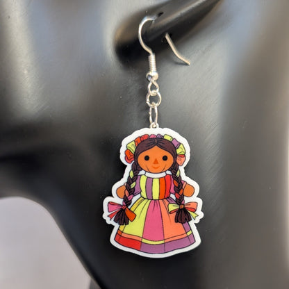 Close-up of a colorful Muñeca Mexican doll acrylic dangle earring with braided hair and a bright traditional dress.