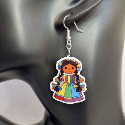 Close-up of a colorful Muñeca Mexican doll acrylic dangle earring with braided hair and a bright traditional dress.