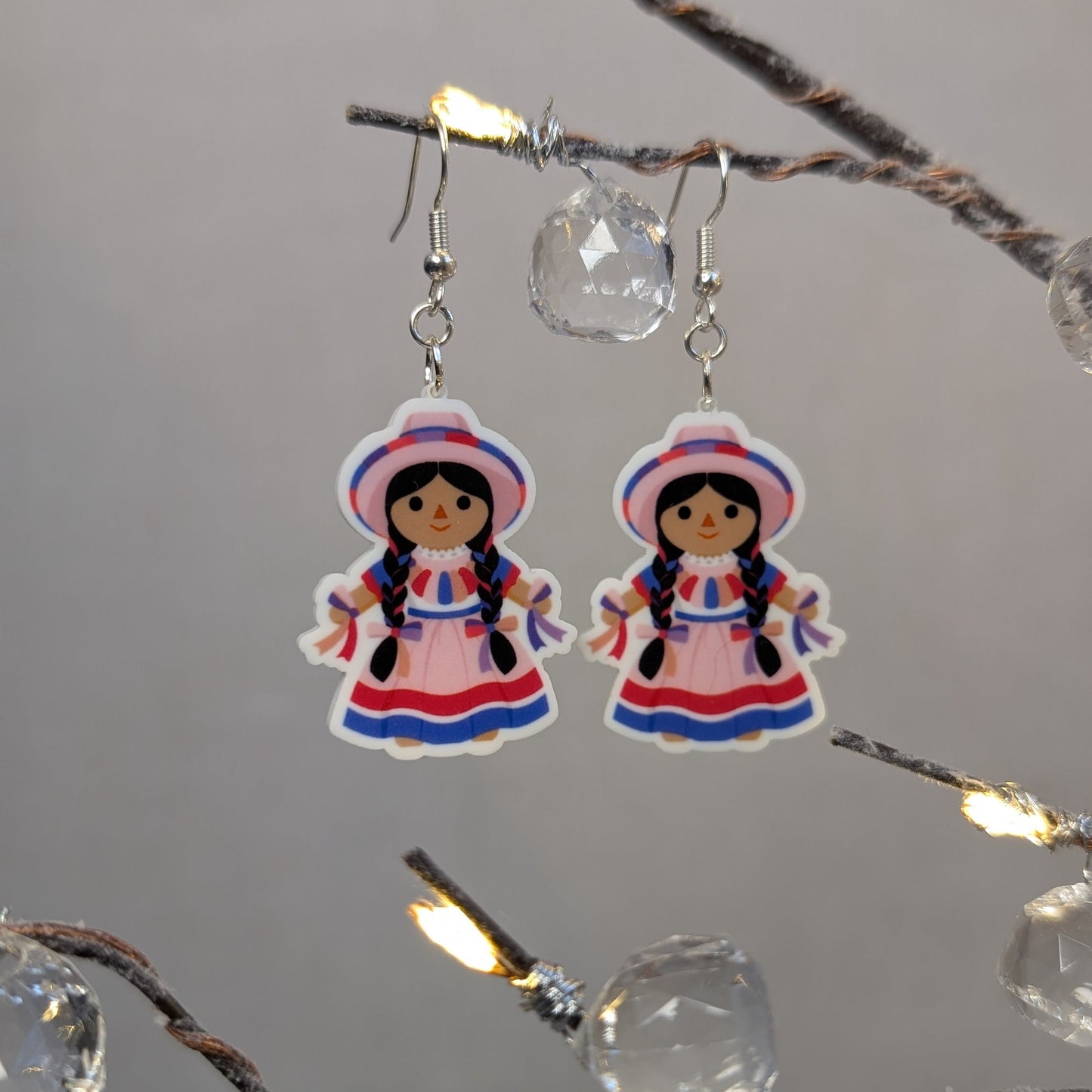 Pair of pink Muñeca Mexican doll acrylic dangle earrings with braided hair, traditional dresses, and matching hats.