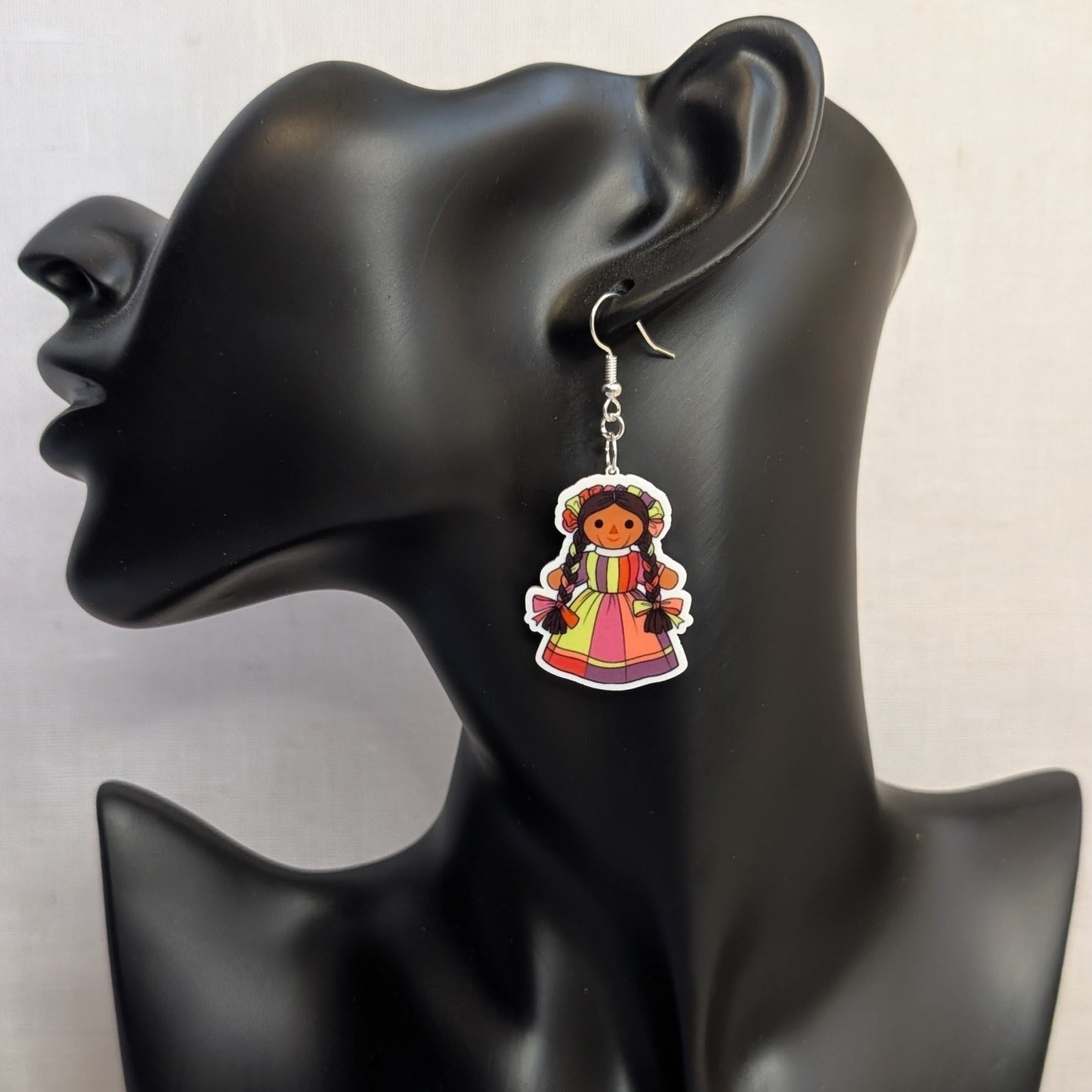 Pink and multicolor Muñeca Mexican doll acrylic dangle earring displayed on a black jewelry stand.