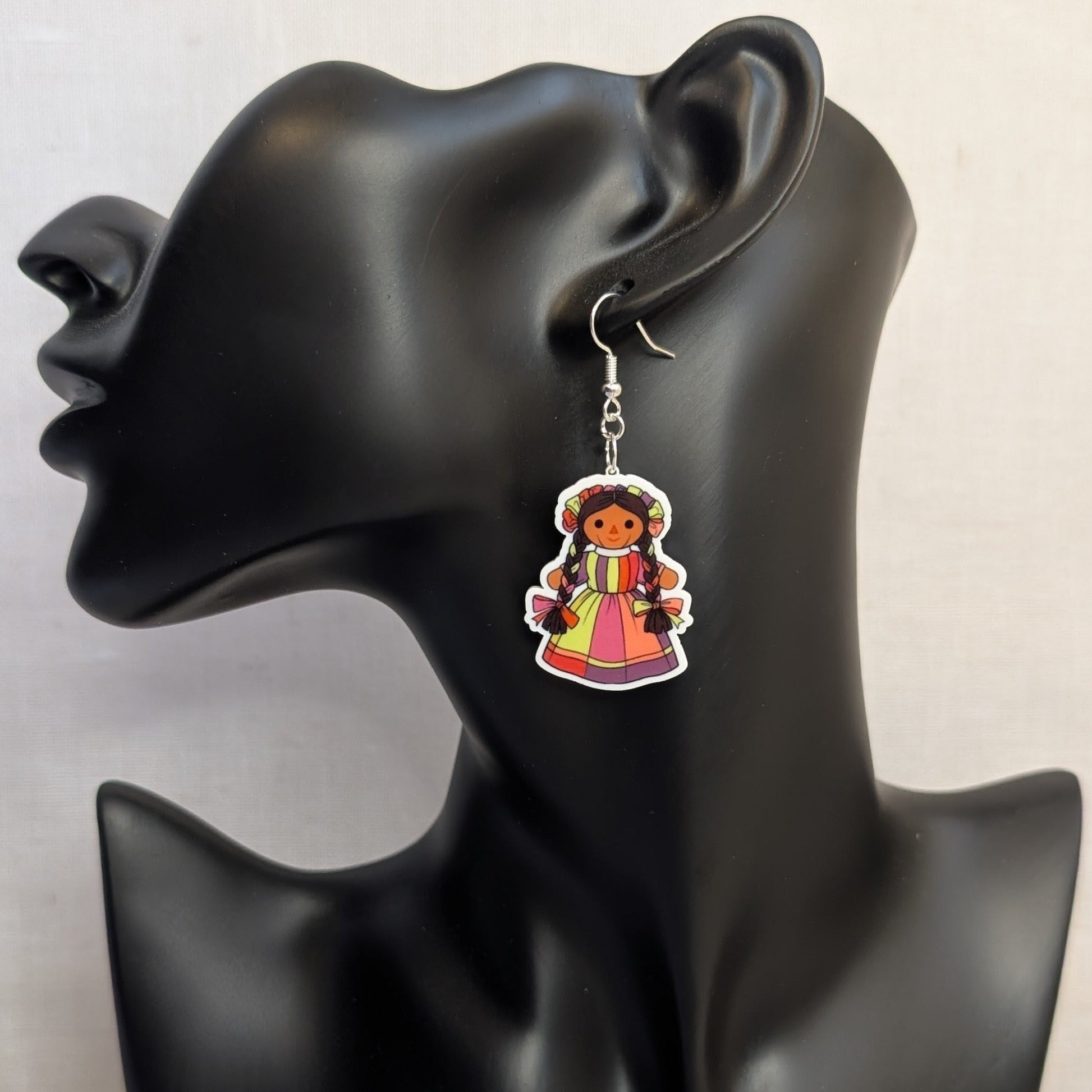 Pink and multicolor Muñeca Mexican doll acrylic dangle earring displayed on a black jewelry stand.