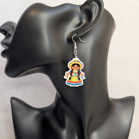 Colorful Muñeca Mexicana doll dangle earring displayed on a black jewelry stand, featuring a traditional Mexican dress and hat.