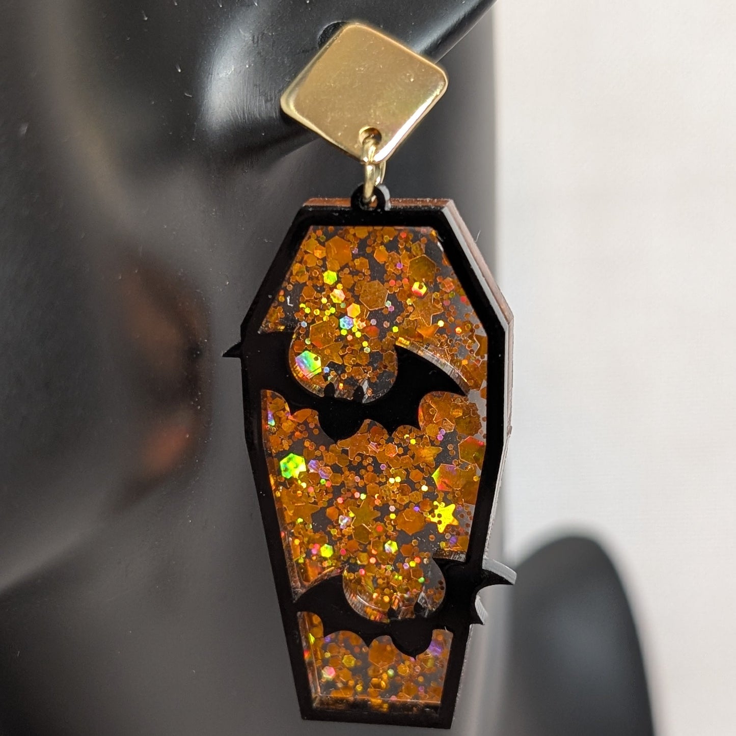 Orange glitter coffin-shaped dangle earring with black bat cutouts, handmade Halloween statement jewelry.