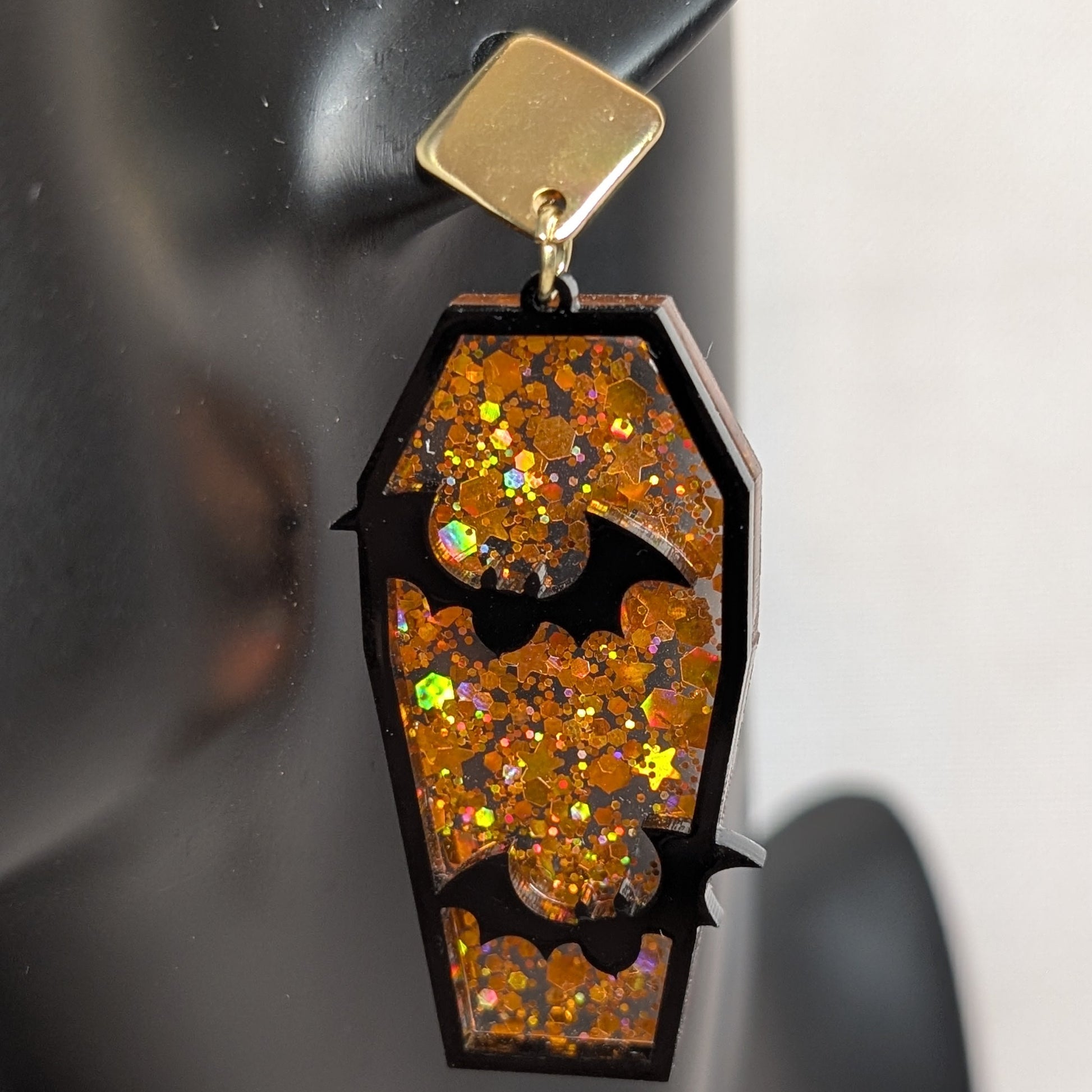 Orange glitter coffin-shaped dangle earring with black bat cutouts, handmade Halloween statement jewelry.