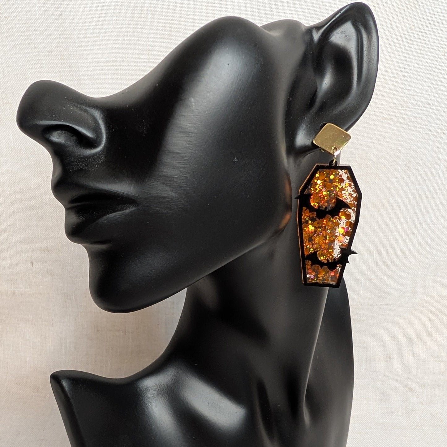 Orange glitter coffin-shaped Halloween earring with black bat cutouts displayed on a black jewelry mannequin.