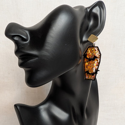 Orange glitter coffin-shaped Halloween earring with black bat cutouts displayed on a black jewelry mannequin.