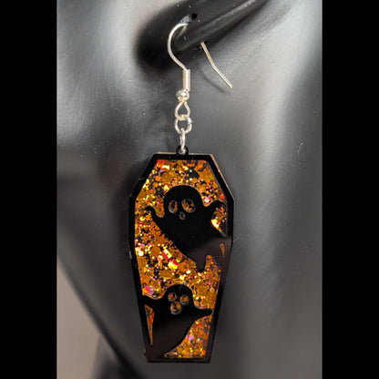 Orange glitter coffin-shaped dangle earring with black ghost cutouts shown in a close-up product view.