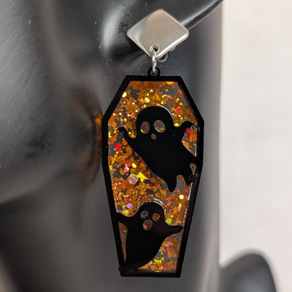Orange glitter coffin-shaped dangle earring with black ghost cutouts, handmade Halloween statement jewelry.