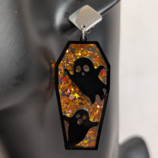 Orange glitter coffin-shaped dangle earring with black ghost cutouts, handmade Halloween statement jewelry.