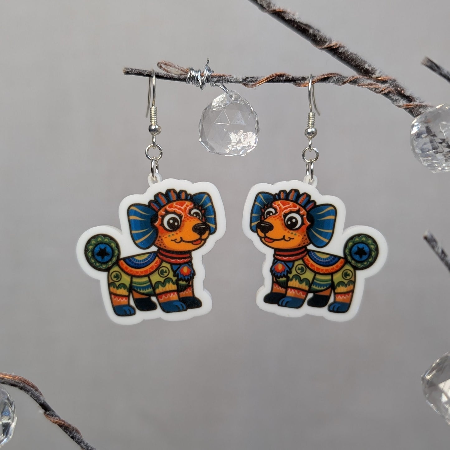 Pair of colorful dog-shaped Alebrije earrings featuring bright Mexican folk art patterns in orange, blue, green, and yellow.