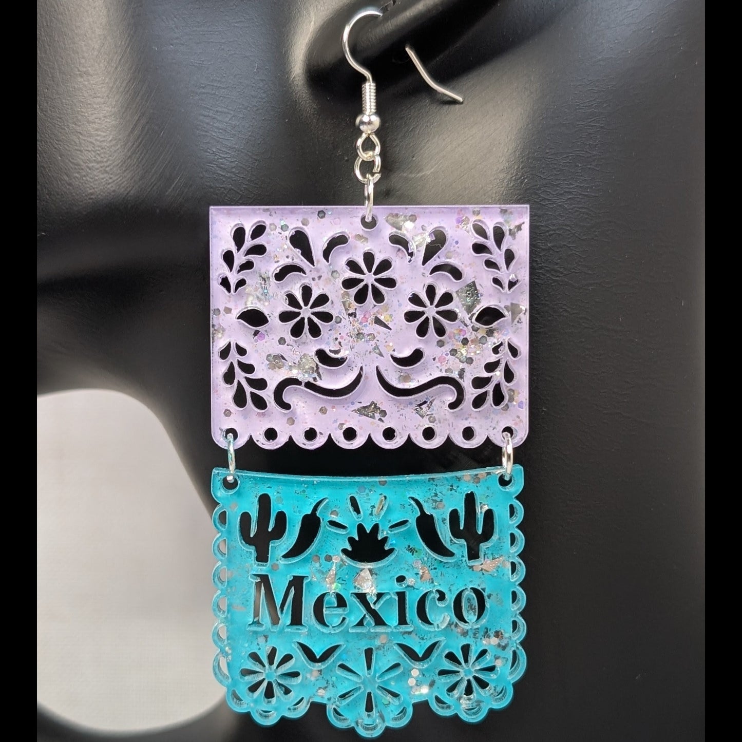 Close-up of turquoise and pink Papel Picado Mexico dangle earring with floral cutouts and cactus details.