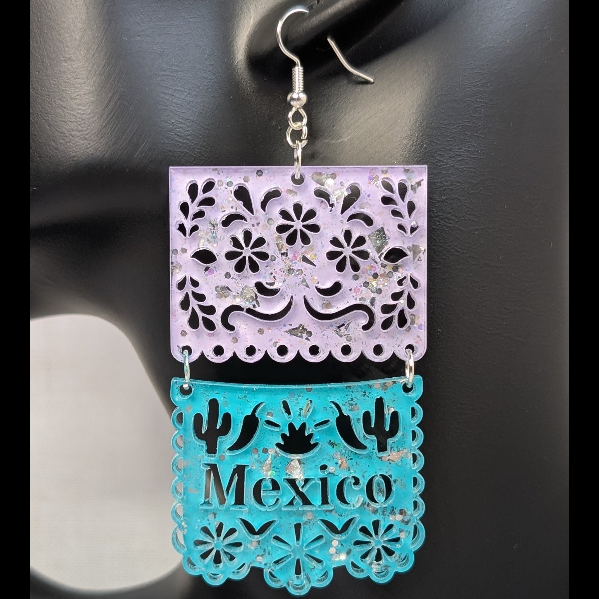 Close-up of turquoise and pink Papel Picado Mexico dangle earring with floral cutouts and cactus details.