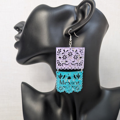 Turquoise and white Papel Picado Mexico dangle earring with floral cutout details displayed on a black jewelry stand.
