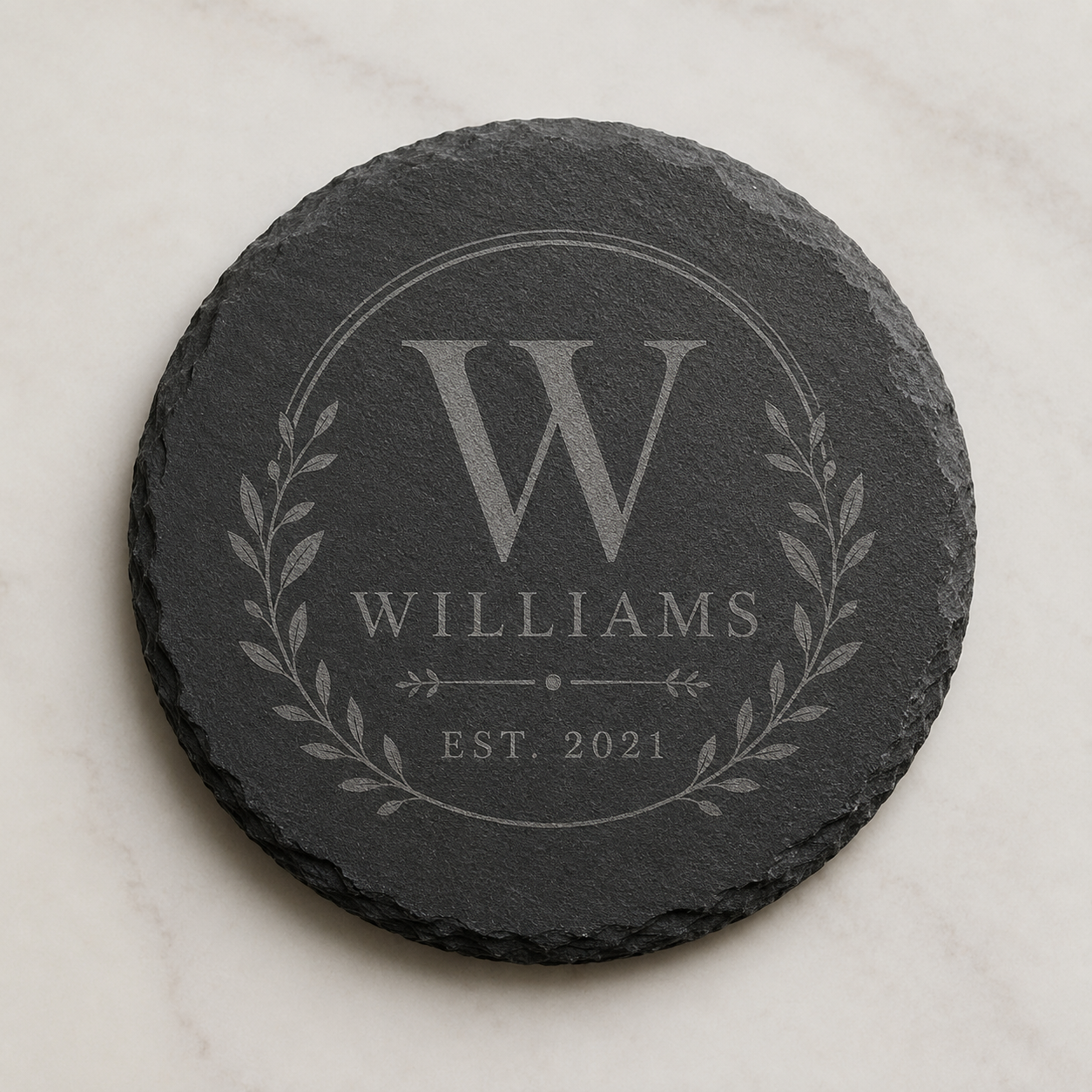 Personalized round slate coaster engraved with a Williams family monogram, laurel design, and established date.