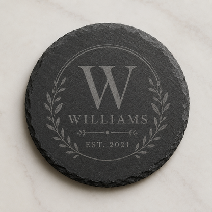 Personalized round slate coaster engraved with a Williams family monogram, laurel design, and established date.