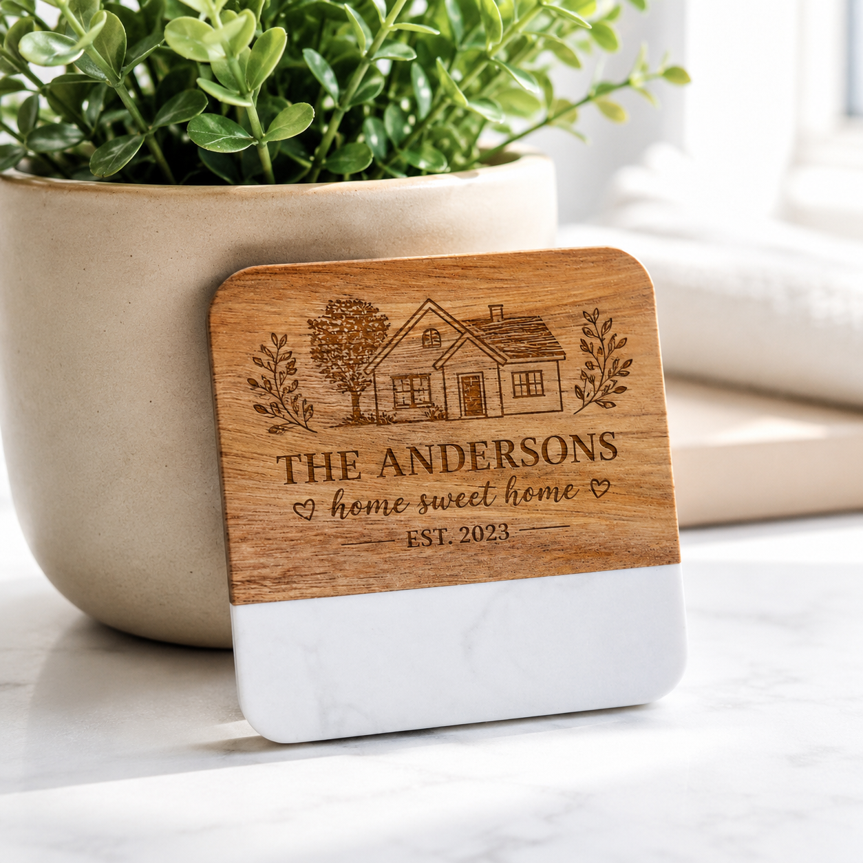 Personalized square marble and acacia wood coaster engraved with the Anderson family name, house illustration, home sweet home message, and established date.