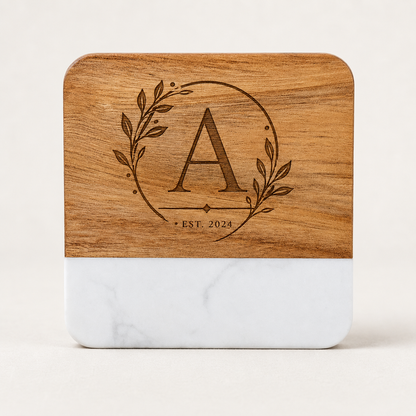 Personalized square marble and acacia wood coaster laser engraved with an elegant botanical monogram and established date.