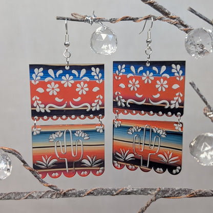 Colorful Serape cactus dangle earrings with red, blue, orange, and white floral patterns and silver cactus charms.