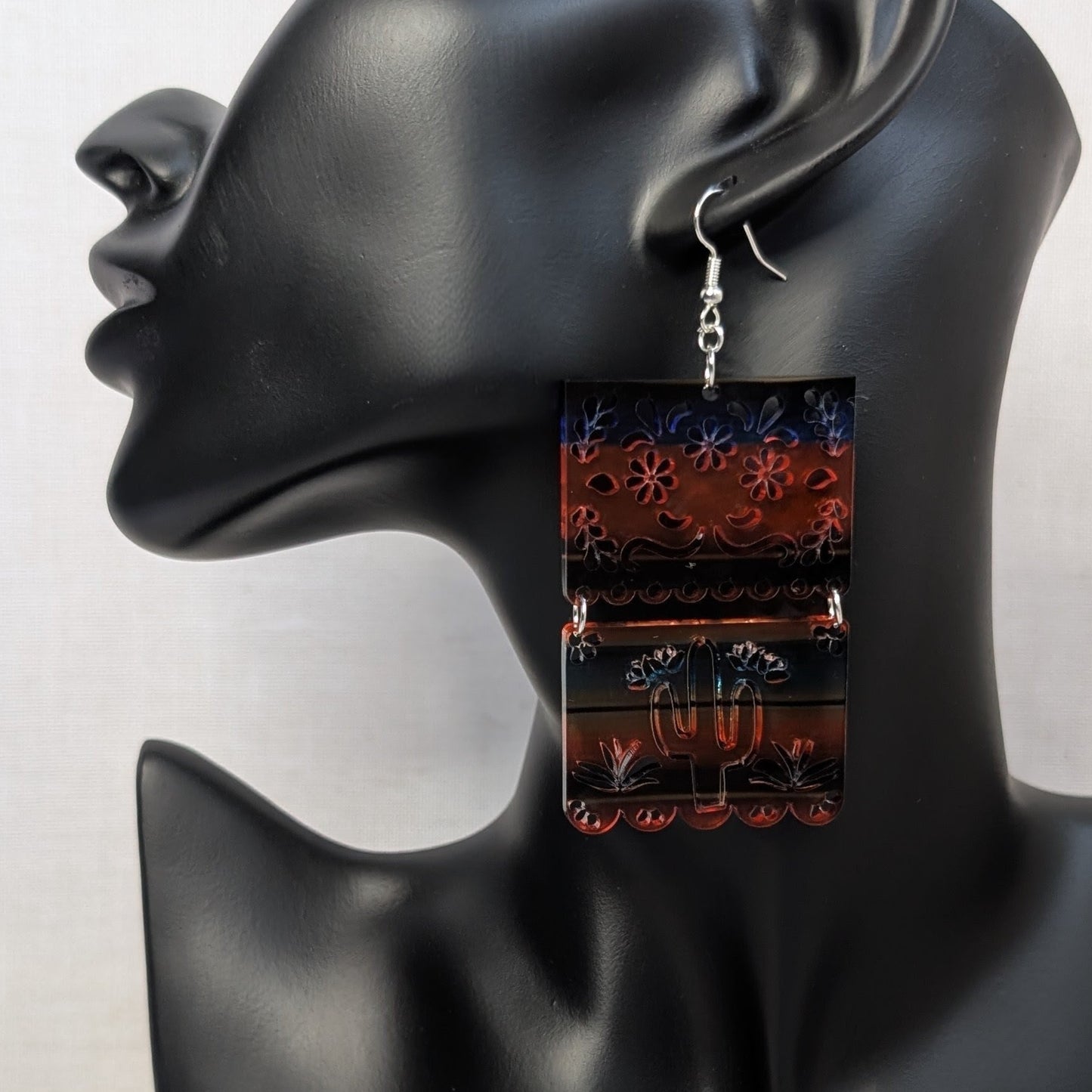 Colorful Serape cactus dangle earring with floral patterns and a silver cactus charm displayed on a black jewelry stand.