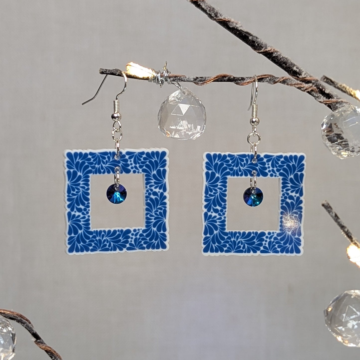 Blue Talavera square earrings with white floral patterns and blue iridescent crystal dangle charms.