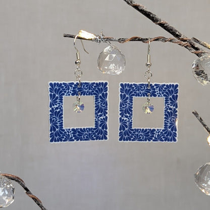 Blue Talavera-style picture frame earrings with white floral patterns and iridescent crystal dangle charms.