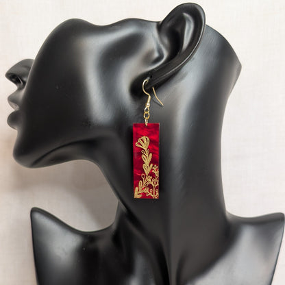 Red rectangular dangle earring from The Gilded Garden Collection with an intricate gold floral design displayed on a black jewelry stand.